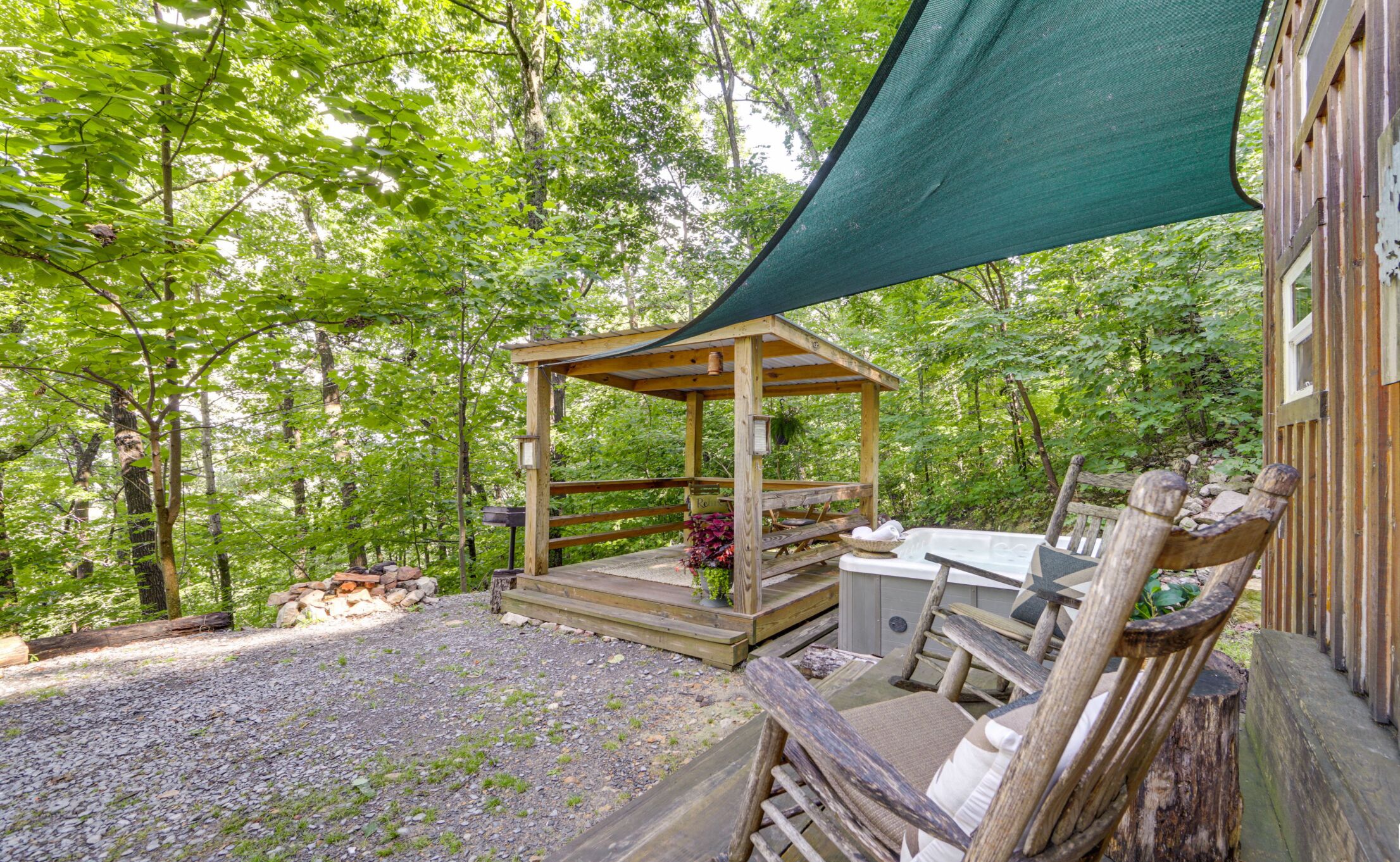Ein hölzernes Gazebo mit Bank und Tisch, umgeben von einem Kiesbereich und Bäumen.