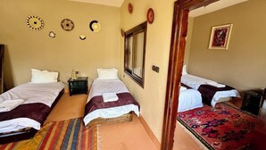 A room with three beds, a wooden door, a mirror, and a red patterned rug.