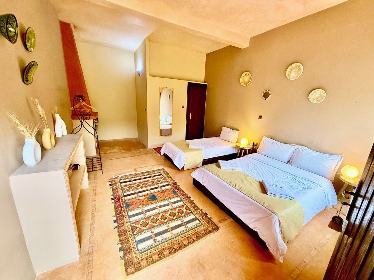 A bedroom with two beds, a desk, a patterned rug, and a door leading to another room.