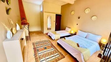 A bedroom with two beds, a desk, a patterned rug, and a door leading to another room.