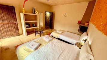 Una habitación con dos camas, una mesita, una estantería con objetos decorativos y una puerta.