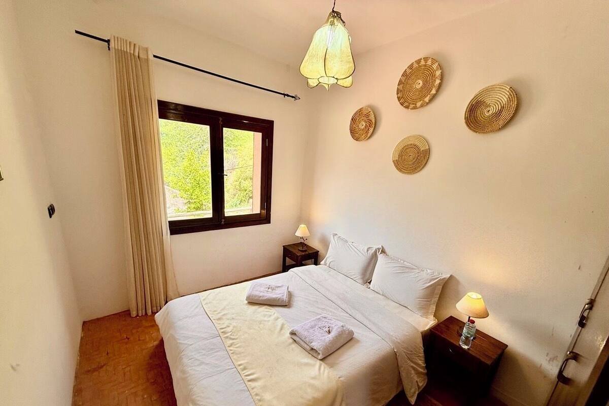 Un dormitorio con una cama, dos mesitas de noche, una ventana con cortinas, una lámpara colgante y decoración en la pared.