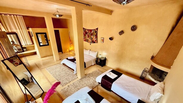A hotel room with three beds, a desk, a chair, a mirror, and a wall-mounted artwork.