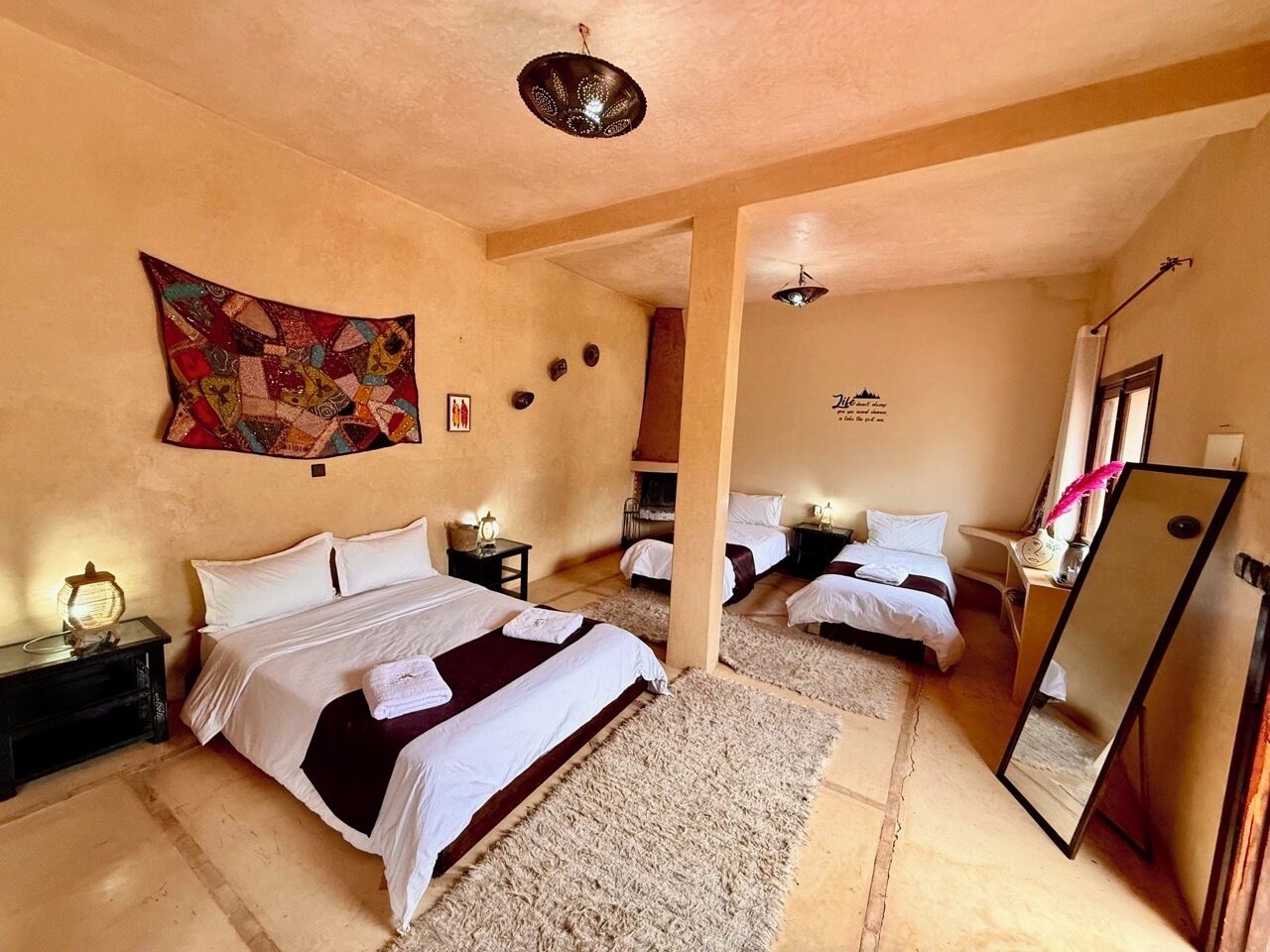 Habitación de hotel con una cama grande, una cama más pequeña, un espejo, una chimenea y un cuadro en la pared.