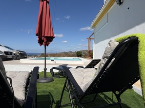 A poolside area with lounge chairs, a red umbrella, and a view of the ocean. - Cortijo del Verdial by At Home Costa del Sol (Torrox)