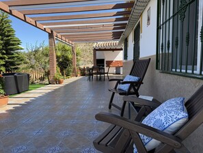 Eine überdachte Terrasse mit einer Pergola, Sitzmöbeln und einer Küchenzeile.
