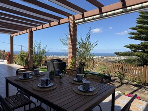 A covered patio with a table set for two, outdoor seating, and a view of the sea. - Cortijo del Verdial by At Home Costa del Sol (Torrox)