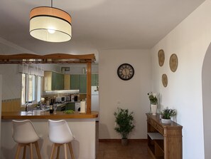 Eine Küche mit einer Holzauslage, zwei weißen Stühlen, einer Pendelleuchte, einer Uhr und Wanddekoration.