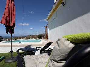 A poolside area with lounge chairs and an umbrella, a white wall, and a view of the sea. - Cortijo del Verdial by At Home Costa del Sol (Torrox)