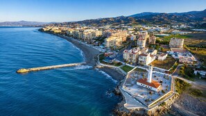 An aerial view of a coastal city with a prominent lighthouse, beachfront buildings, and a rocky breakwater. - Cortijo del Verdial by At Home Costa del Sol (Torrox)