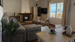 Una sala de estar con un sofá, una chimenea, un televisor y un comedor con una mesa y sillas.