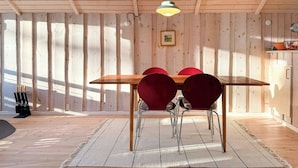 Een kamer met houten lambrisering, een eettafel met stoelen, een hanglamp en een ingelijst schilderij aan de muur.