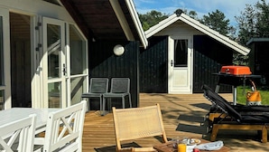Een houten terras met buitenmeubilair, zoals een tafel, stoelen en een barbecuehoek.