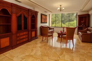 A spacious room with a large wooden cabinet, two chairs, a table, and a large window with a view of greenery. - Ideal for large groups : 450 sq. mts. apartment : Jacuzzi +2 parking spaces (Guayaquil)
