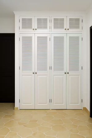 Un conjunto de puertas dobles blancas con listones horizontales, una puerta negra a la izquierda y un suelo con diseño de piedra beige.