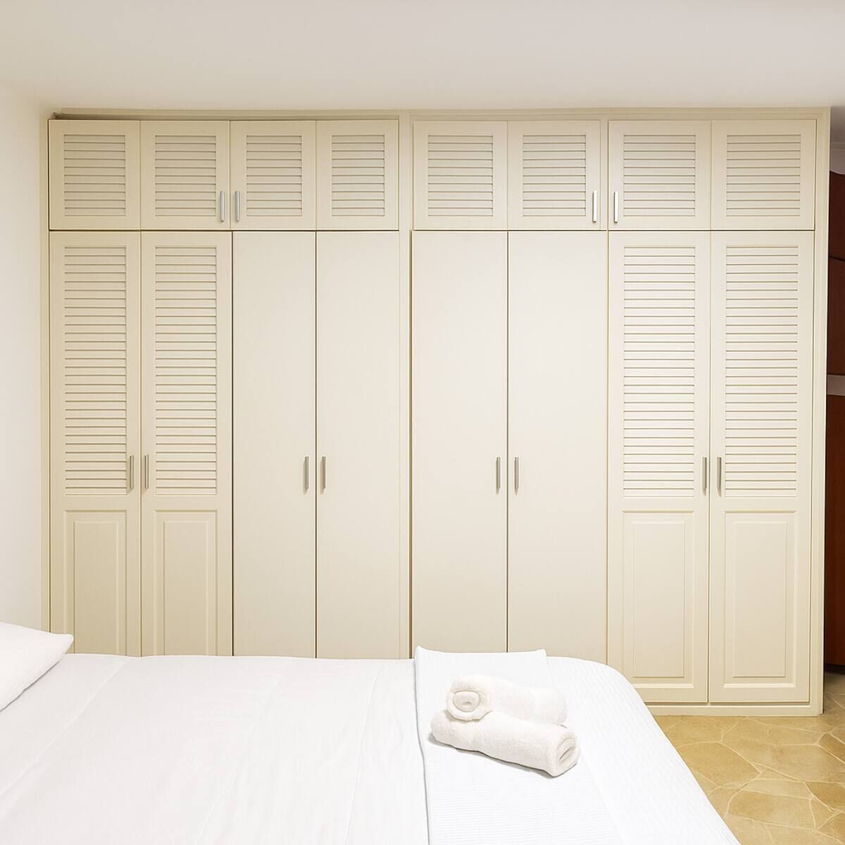 A bedroom with a bed, a white towel, and a large wardrobe with multiple doors.