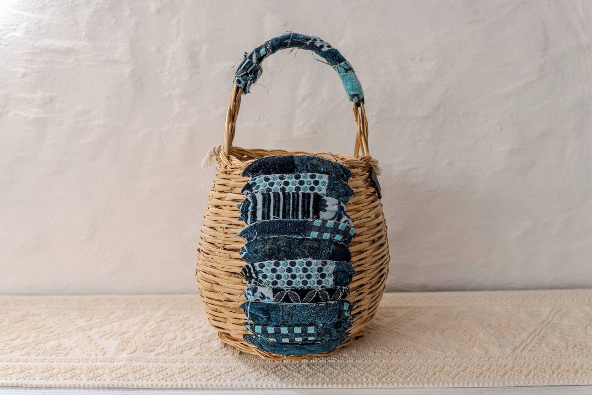 A woven basket with a handle, placed on a textured surface.