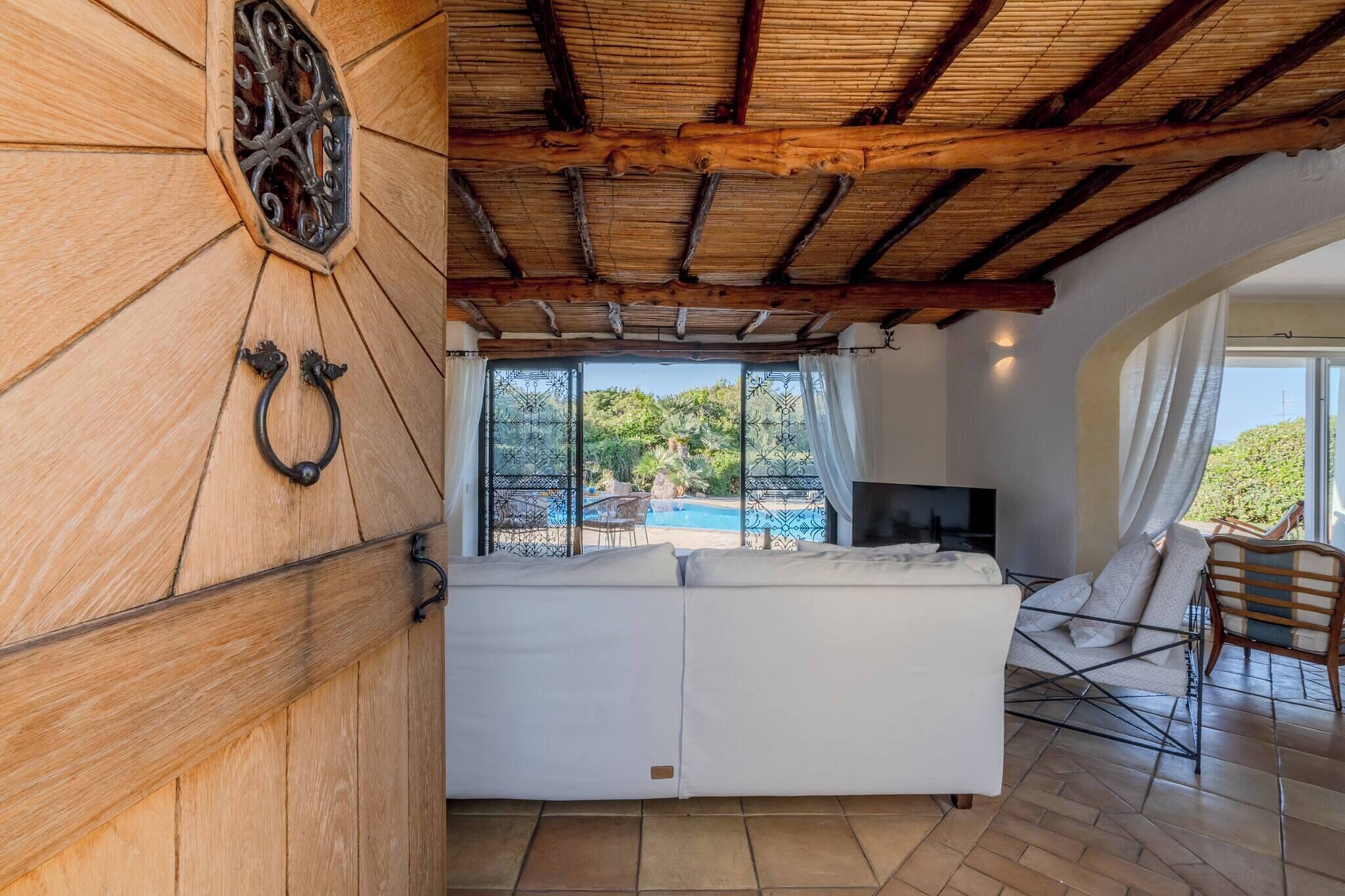 A room with a wooden ceiling, a large window overlooking a pool, a white sofa, and a TV.