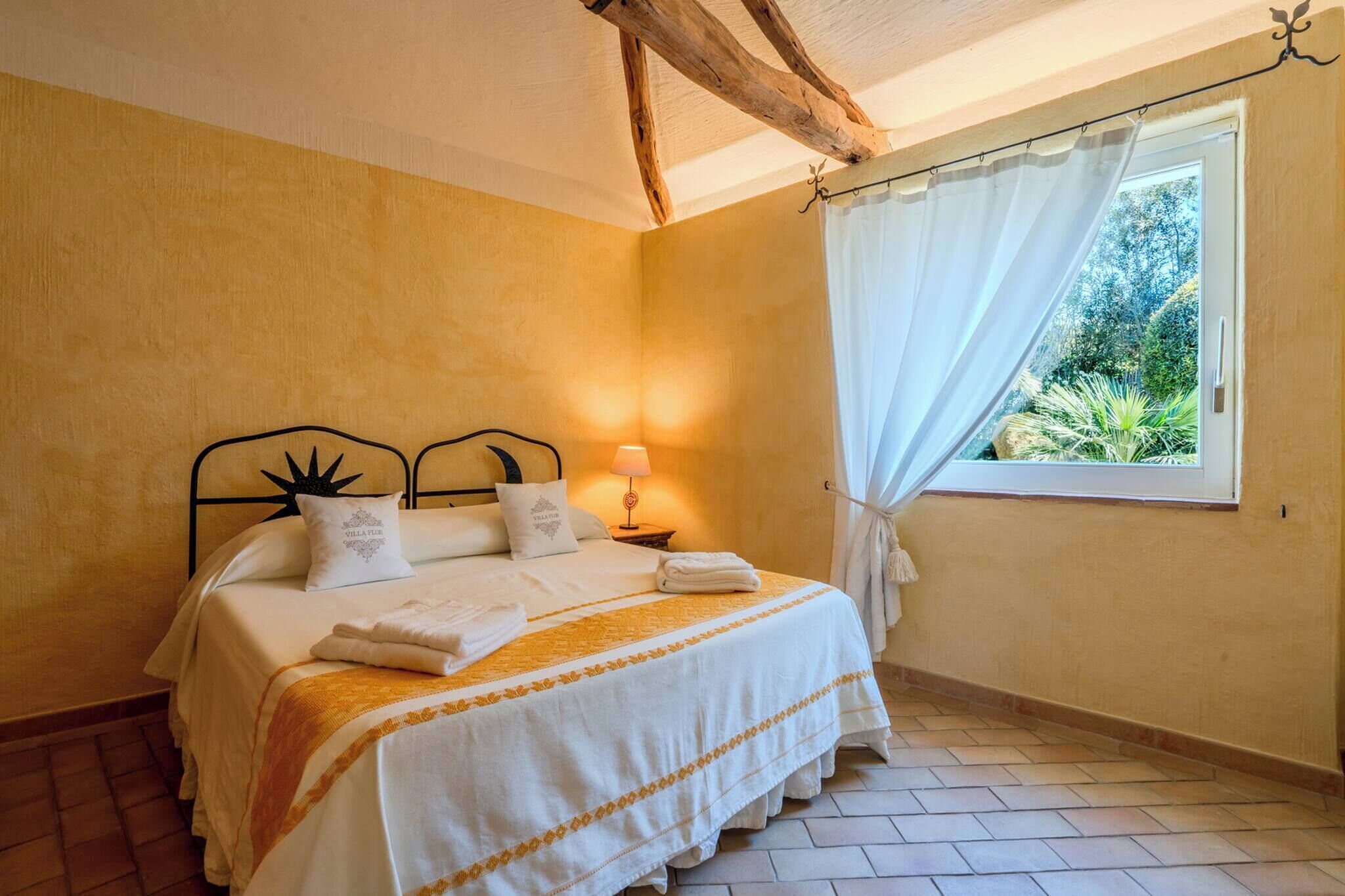 A bedroom with a bed, a nightstand, a window with curtains, and a view of greenery outside.