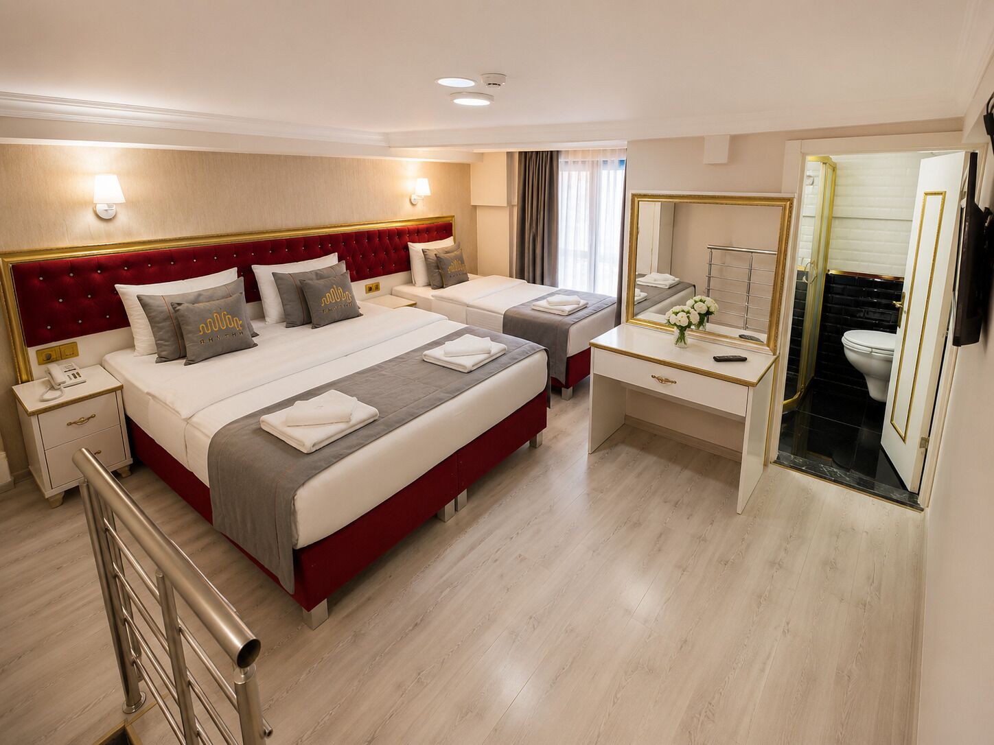 A hotel room with two beds, a desk, a mirror, a telephone, and a bathroom visible through an open door.