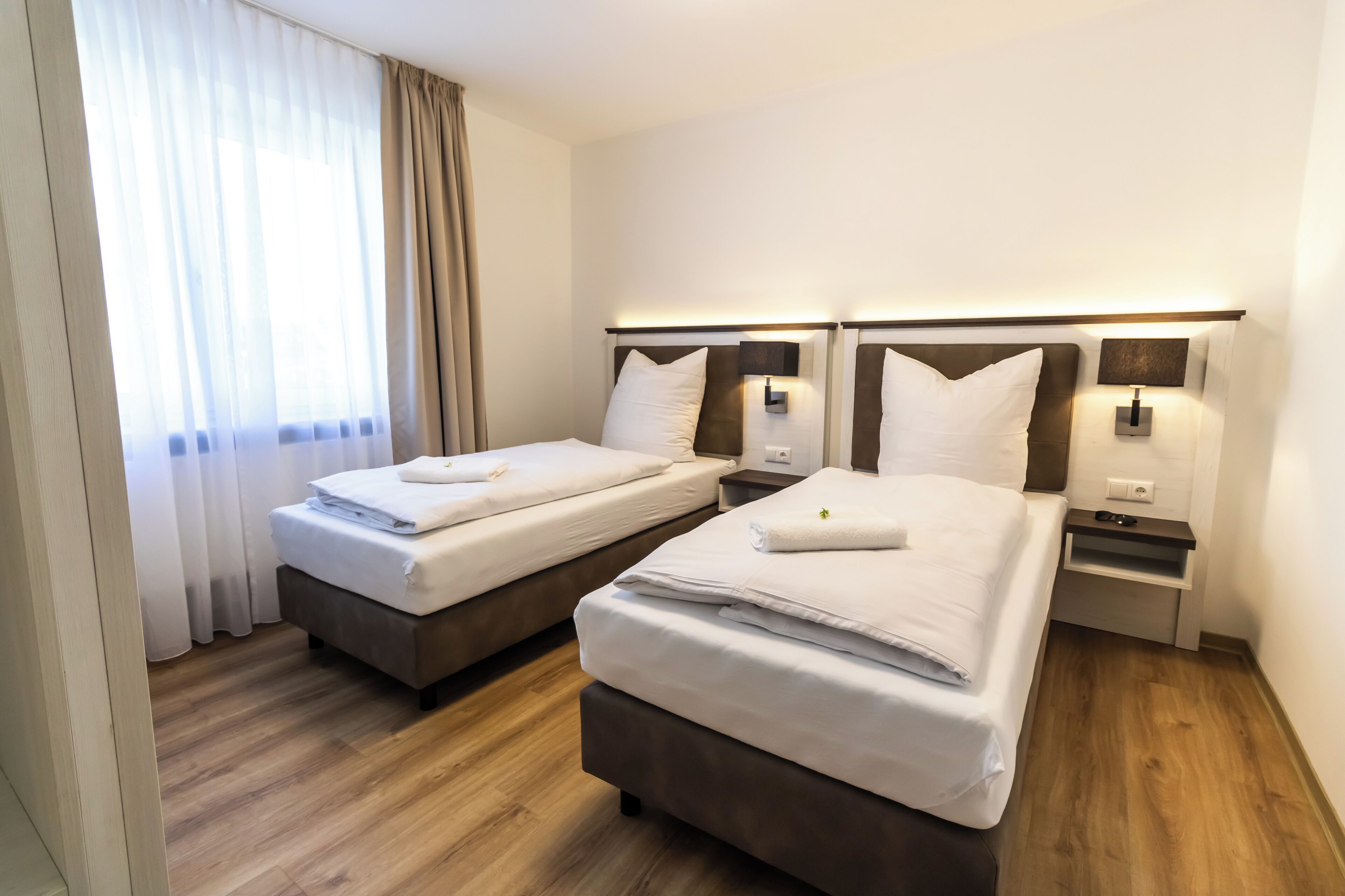 Una habitación de hotel con dos camas, suelo de madera y una ventana con cortinas.
