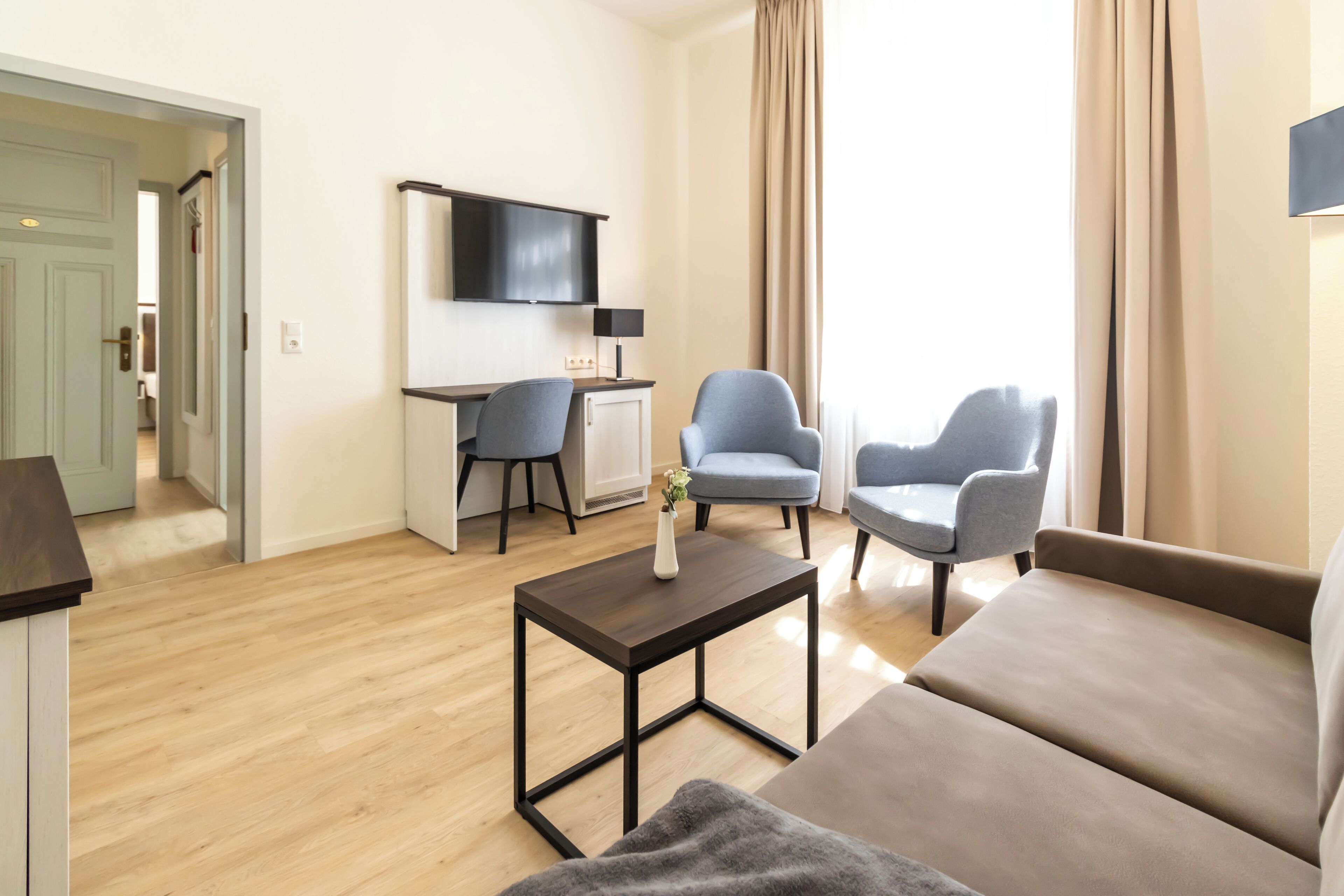 A modern living room with a sofa, two armchairs, a coffee table, a TV, and a desk.