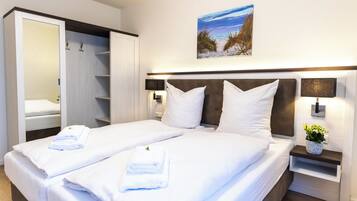 Une chambre d’hôtel avec un lit, une armoire, une table de chevet avec une plante et un tableau au mur.