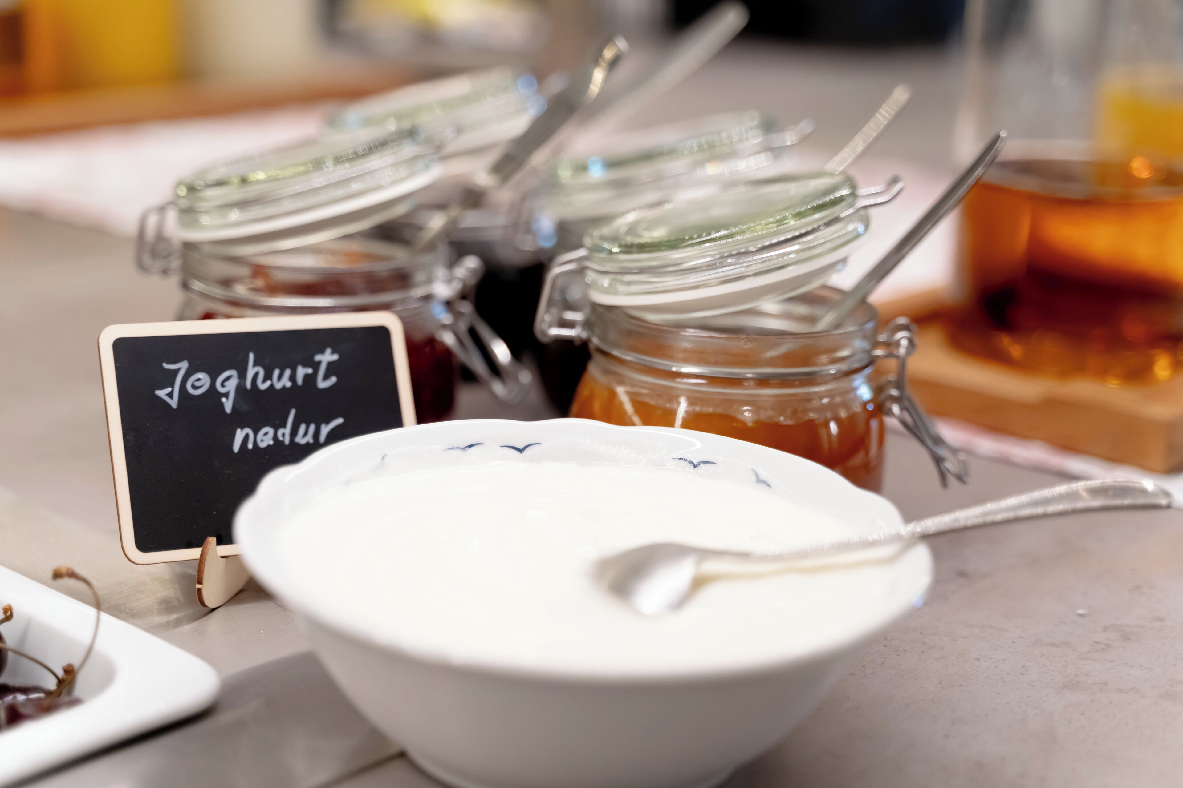 Een assortiment potjes yoghurt en honing, met een bordje met de tekst 'Yoghurt nadur'.