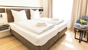 Una habitación de hotel con dos camas, una mesita con una planta y una mesita de noche con lámpara.