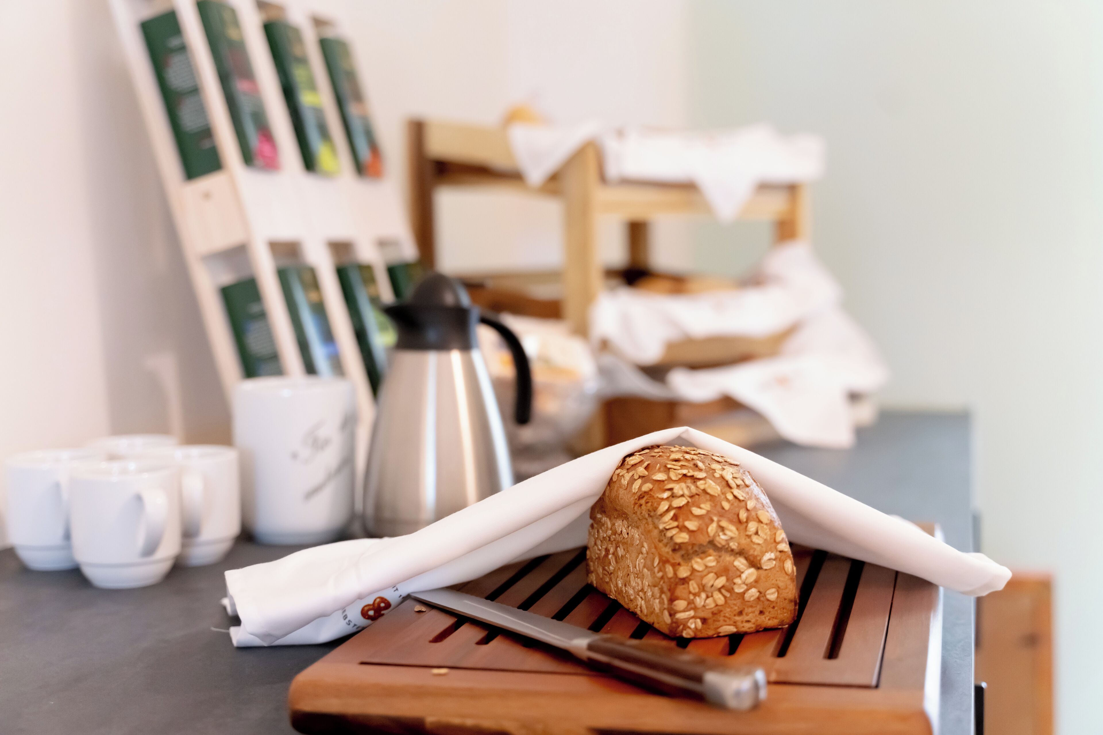 A loaf of bread on a wooden board, a knife, and a coffee maker in a kitchen setting.