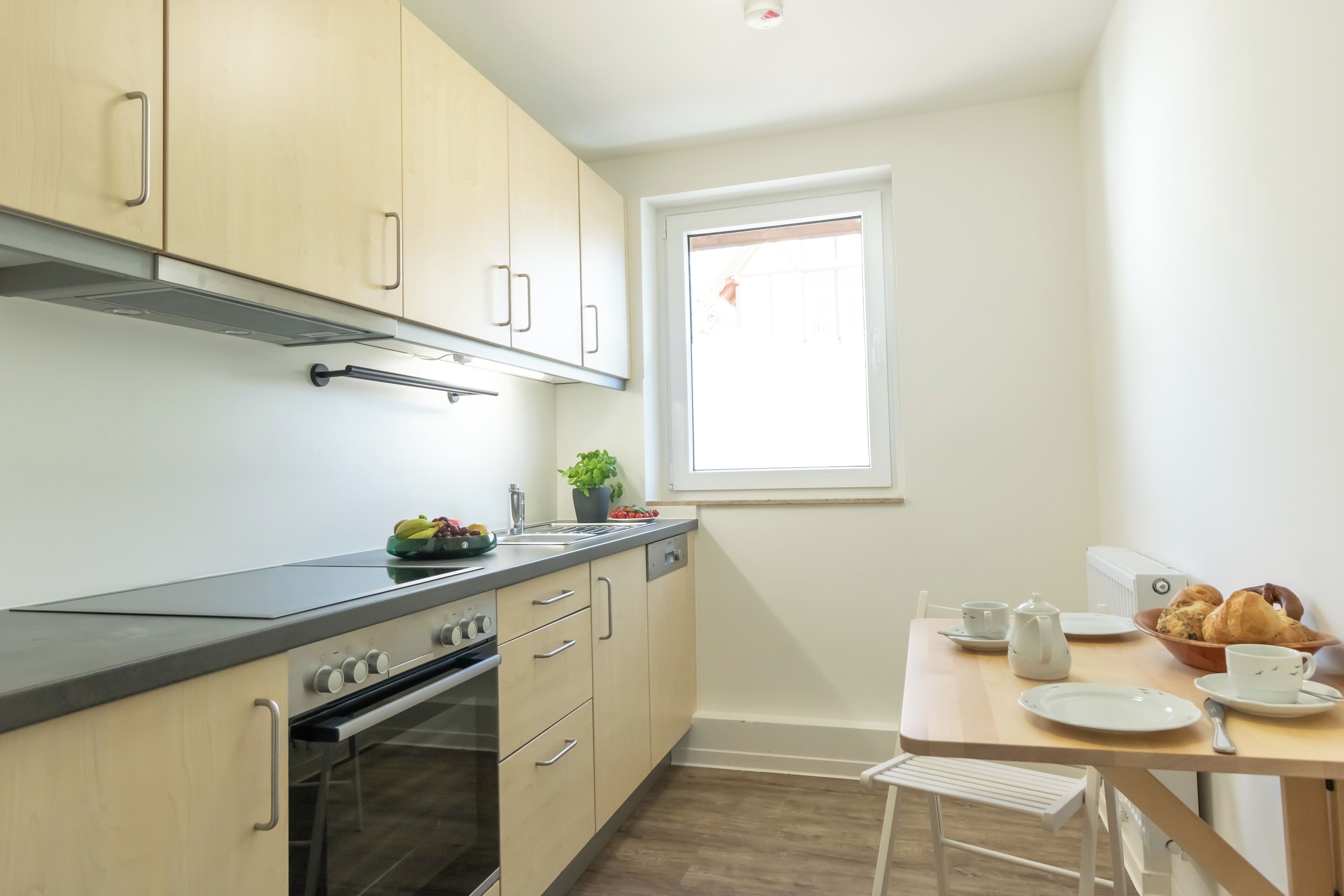 A modern kitchen with wooden cabinets, a built-in oven, a sink, and a dining area with a table and chairs.