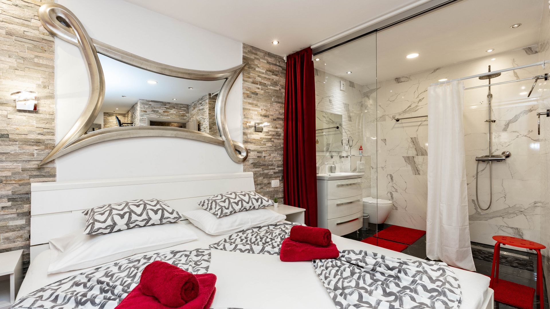 Habitación de hotel moderna con una cama grande, baño con ducha y un espejo de diseño único.