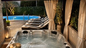 Ein Whirlpool mit Liegestühlen, ein Schwimmbad und eine Gartenanlage.