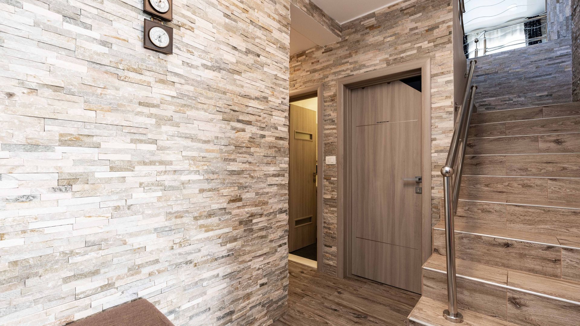 A hallway with a stone wall, a wooden door, and a wooden staircase.
