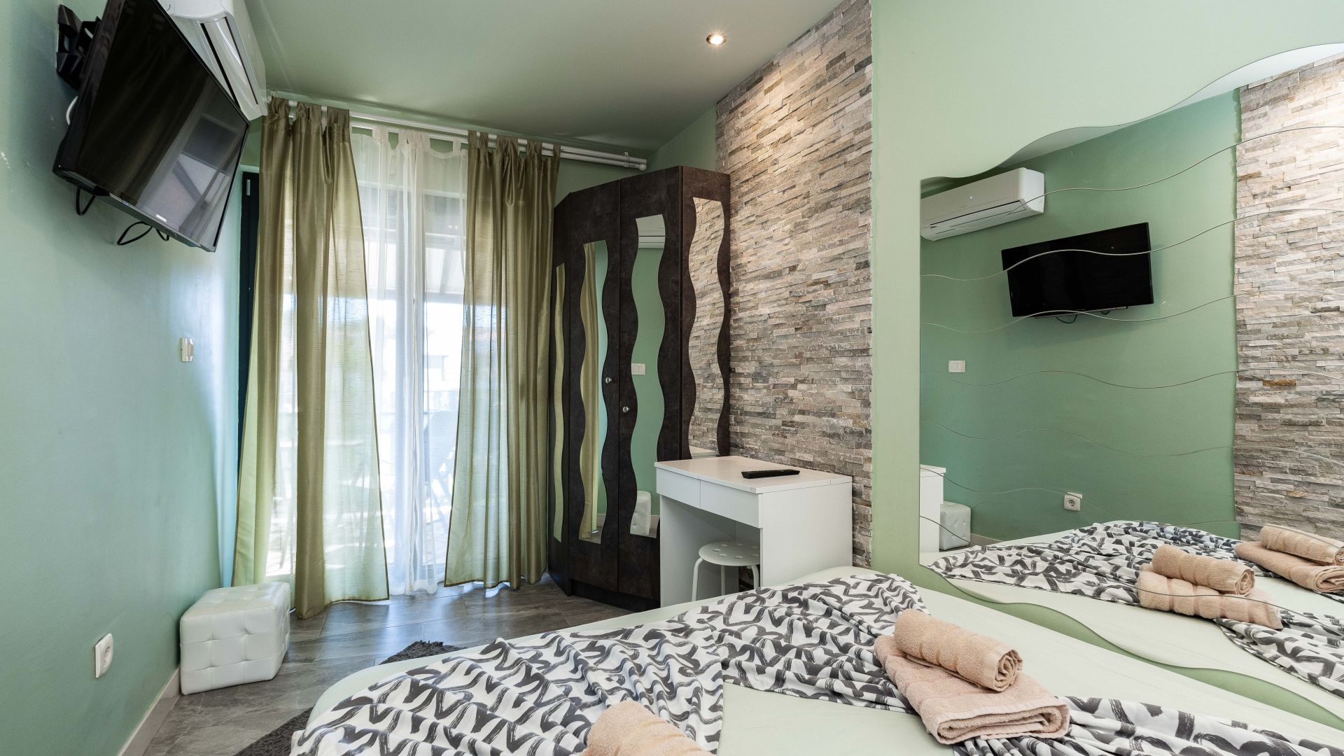 A hotel room with a bed, a desk, a chair, a television, and a bathroom with a shower curtain.