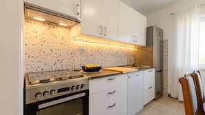 Eine moderne Küche mit Gaskochfeld, Backofen, weißen Schränken, einer Spritzschutzleiste mit gemustertem Dekor und einem Fenster mit Vorhängen.
