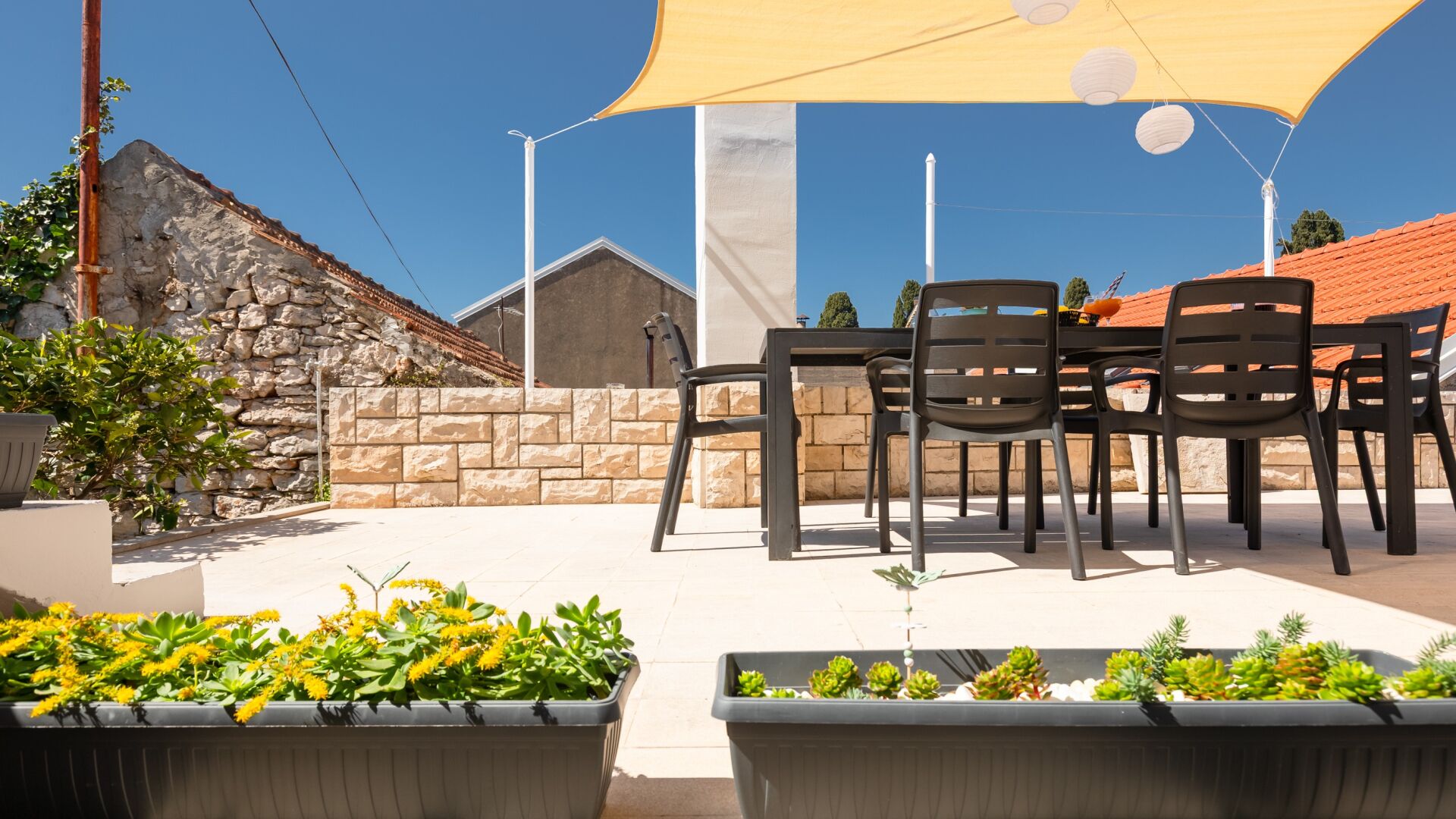Un patio al aire libre con una mesa, sillas, paredes de piedra y plantas en macetas.