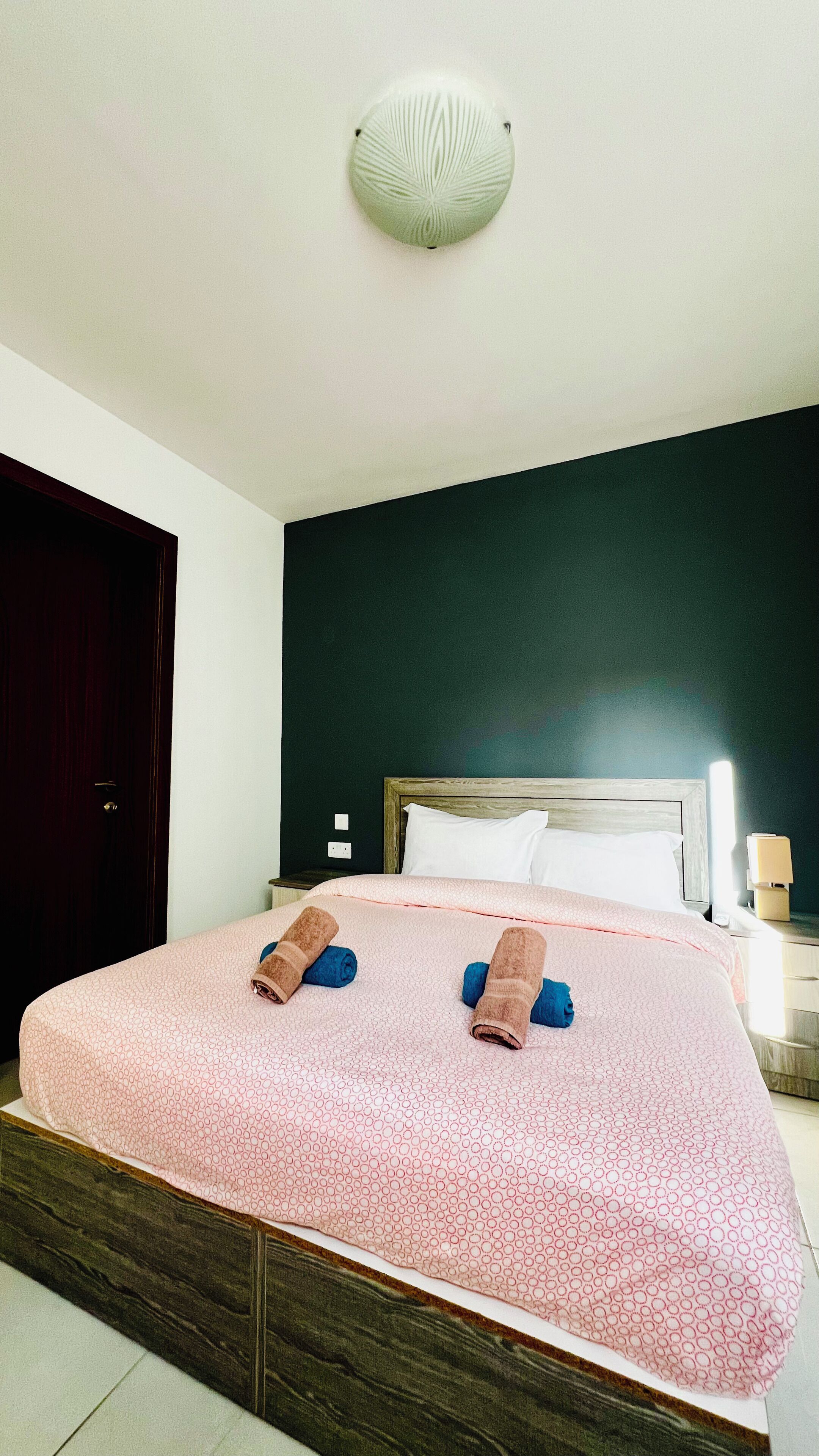 A hotel room with a bed, a wooden headboard, a nightstand, and a wall-mounted light fixture.