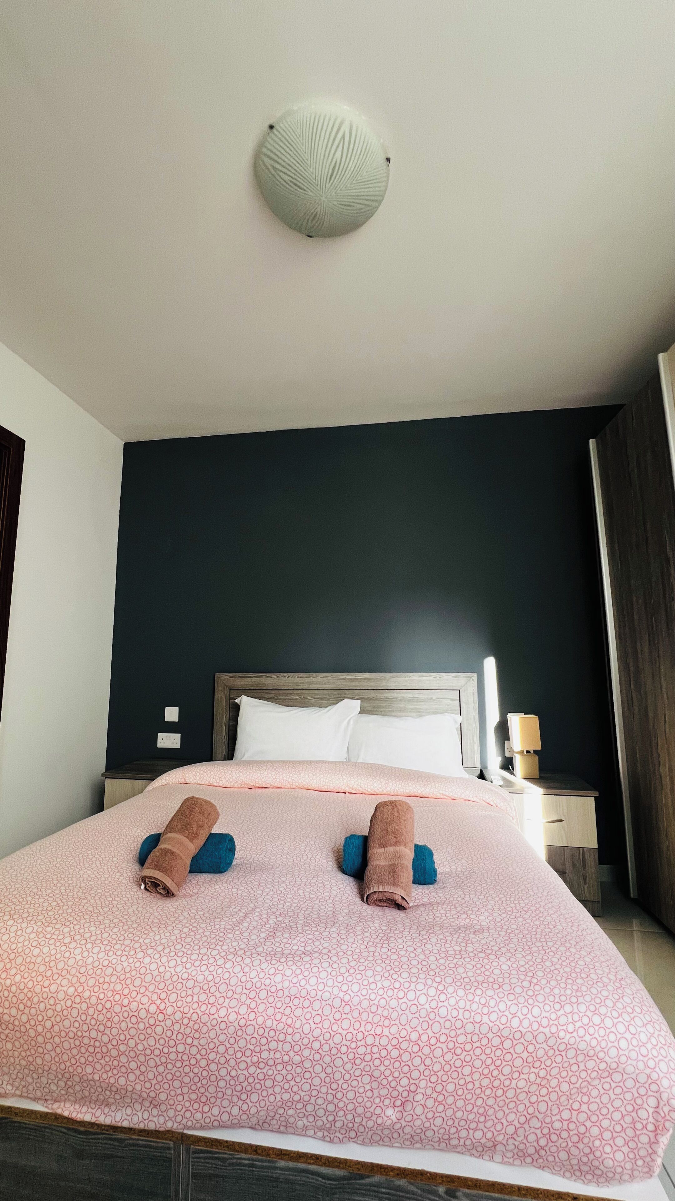 Ein Hotelzimmer mit Bett, Nachttisch, Lampe und Deckenleuchte.