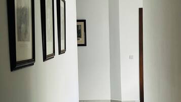 A hallway with white walls, a tiled floor, and framed pictures on the left wall.