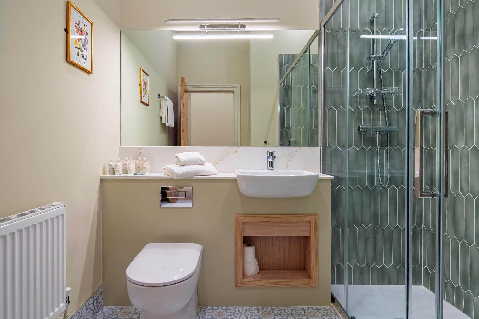 A bathroom with a toilet, sink, shower, and a mirror.