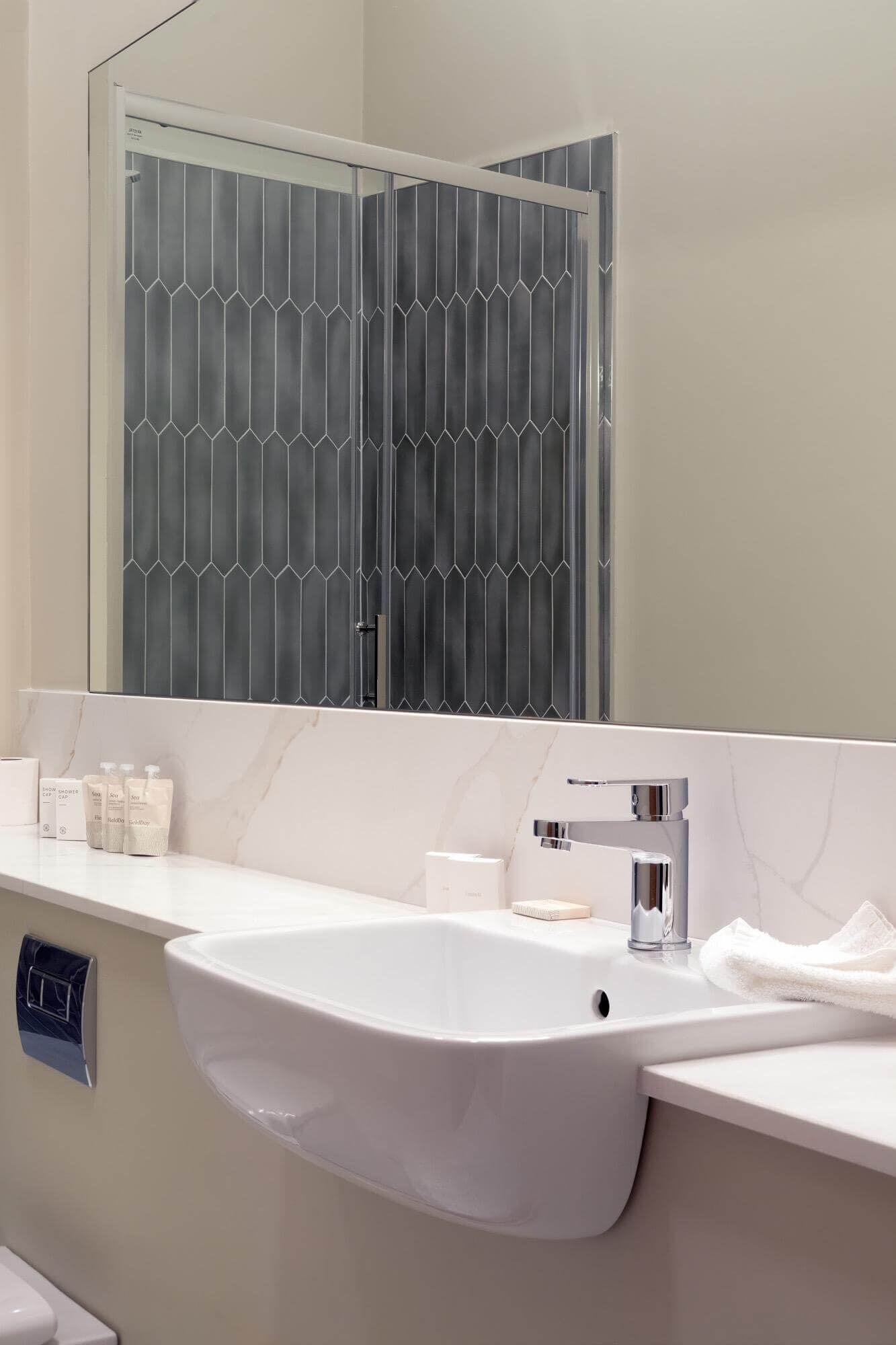 A modern bathroom with a white sink, a large mirror, and a towel rack.