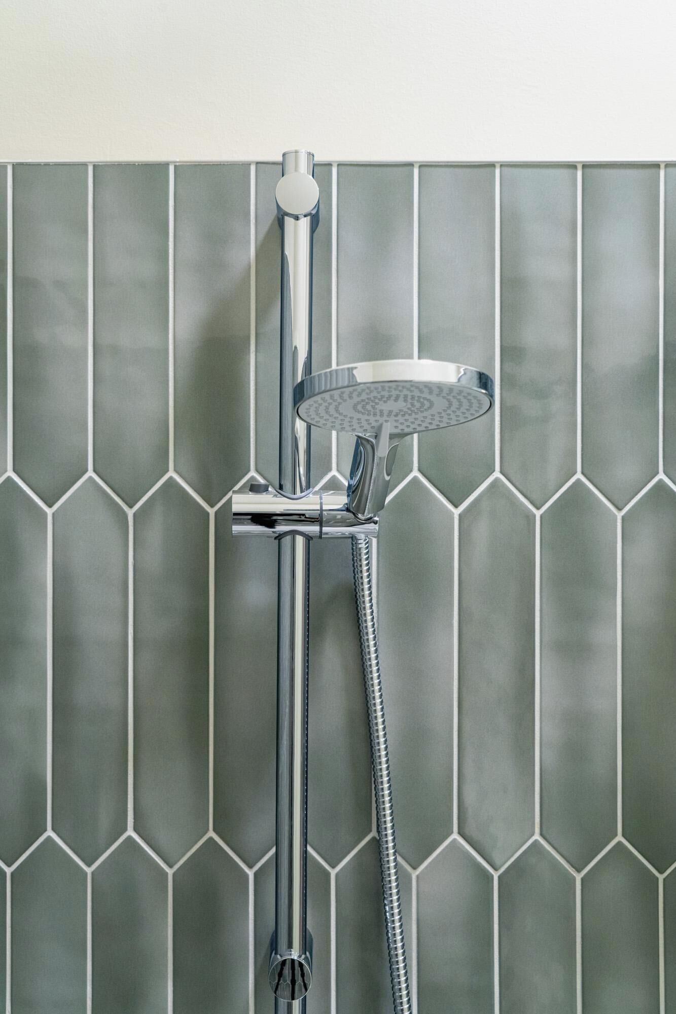 A shower with a handheld showerhead and a wall-mounted control.