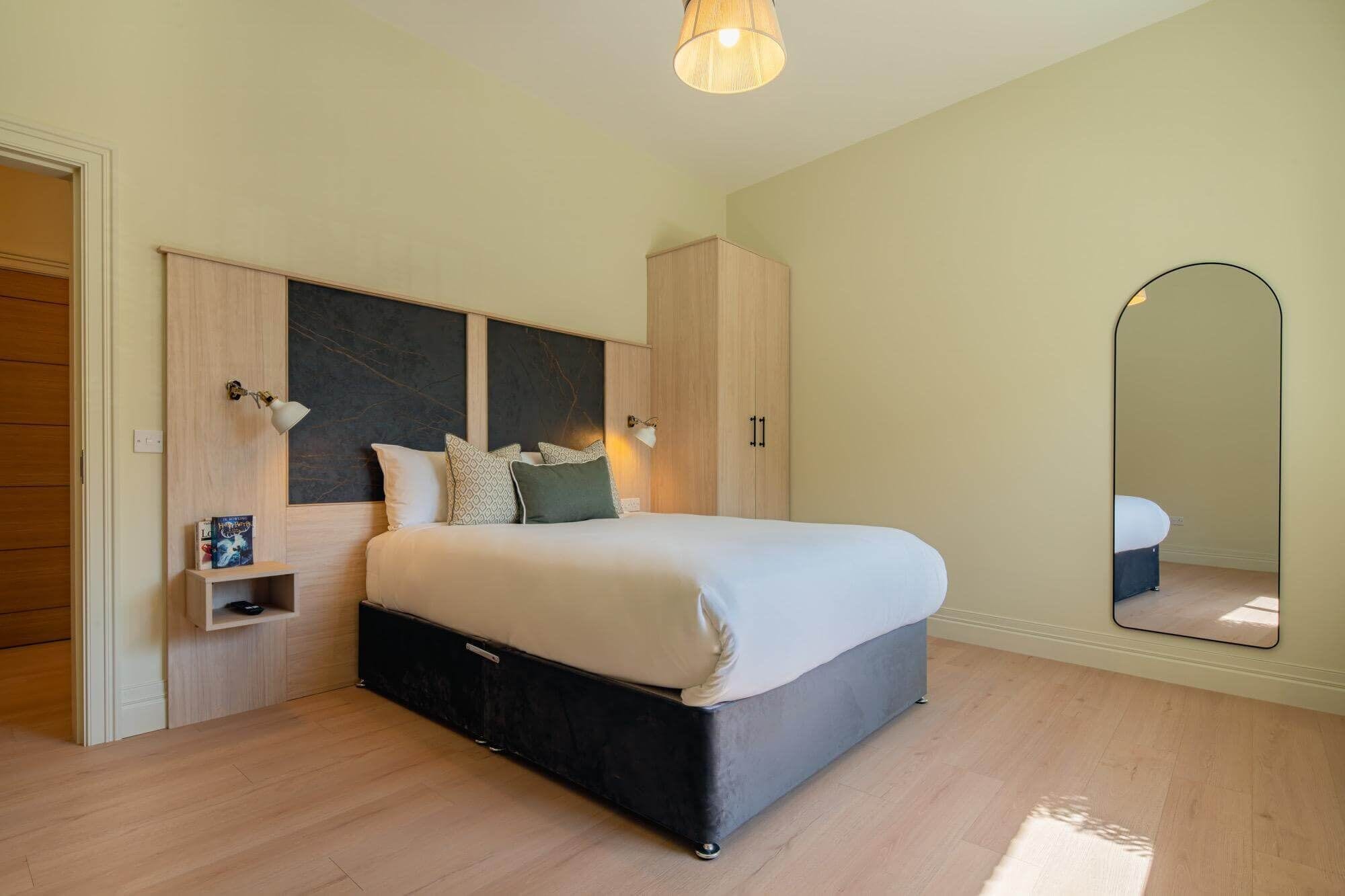 A bedroom with a bed, wardrobe, bedside table, and a mirror.