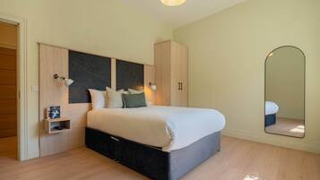 A bedroom with a bed, wardrobe, bedside table, and a mirror.