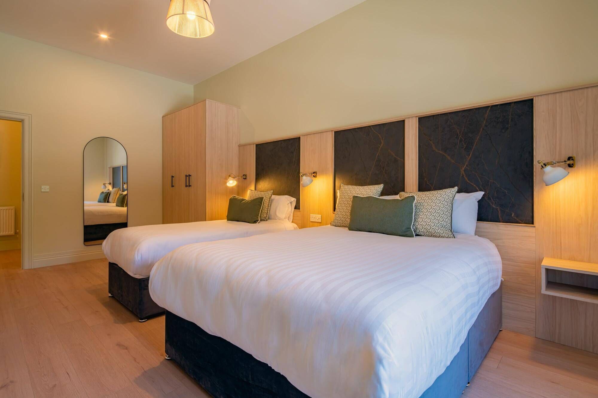Habitación de hotel con dos camas, un espejo grande, armario de madera y lámparas de pared.