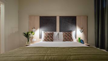 Habitación de hotel con cama, mesita de noche, un florero y una lámpara de pared.