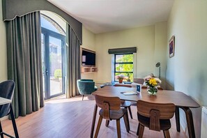 A dining area with a table, chairs, a TV, and a window with a view of greenery.