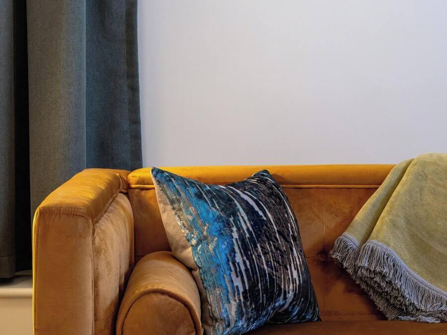 Un sofá marrón con una almohada de estampado azul y una manta verde.