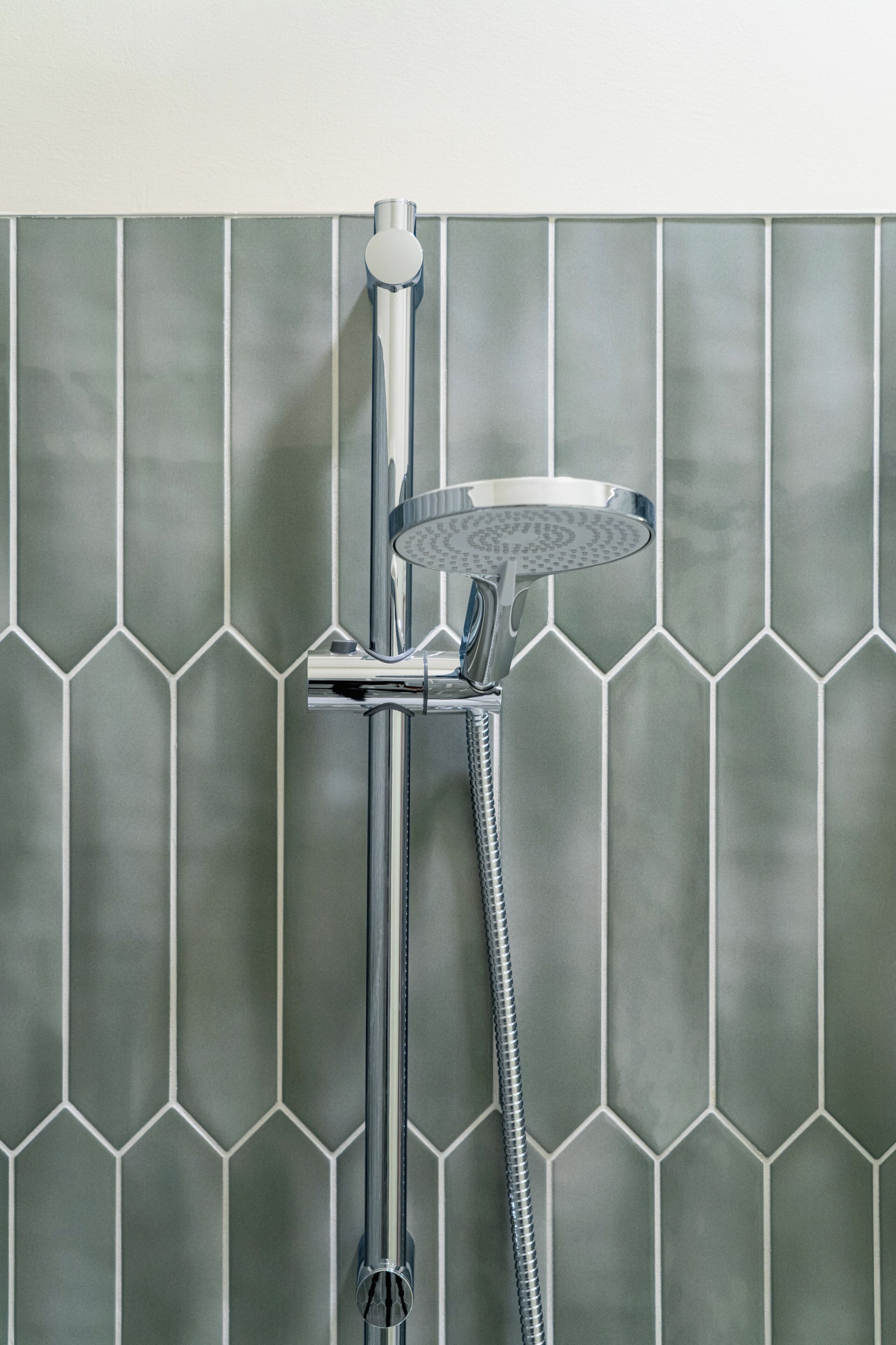 Douche met een handdouche en flexibele slang, bevestigd aan een wand met een mozaïek van zeshoekige tegels.